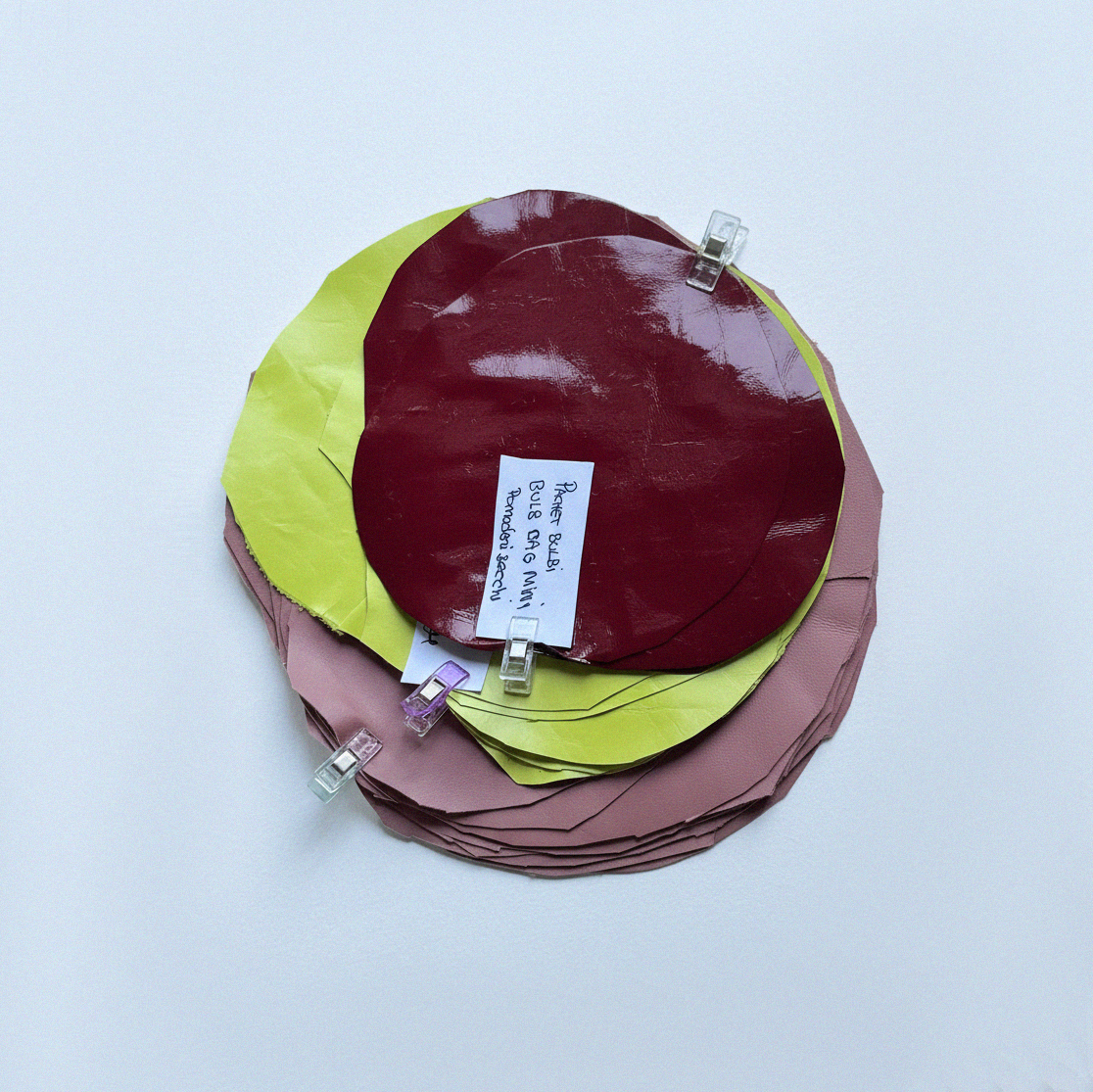 Circular pattern pieces and eco leather samples in red, lime, and nude tones used for The Bulb Bag design process in the Bucharest handmade studio.
