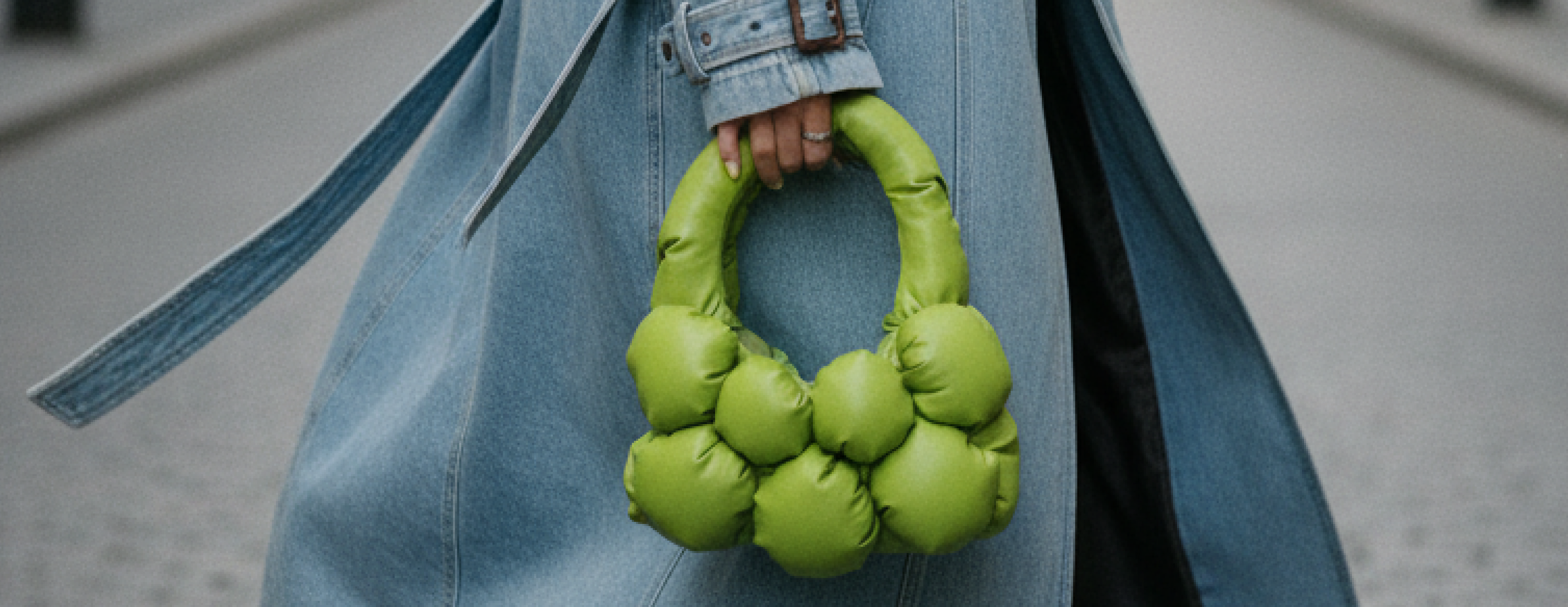 Handmade green Bulb Bag in matte eco-leather, sculptural and puffy, held by a person wearing a denim coat on a city street.