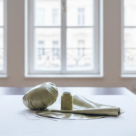 Soft green eco leather, thread, and needle on a white table in natural light during The Bulb Bag handmade crafting process in Bucharest studio.
