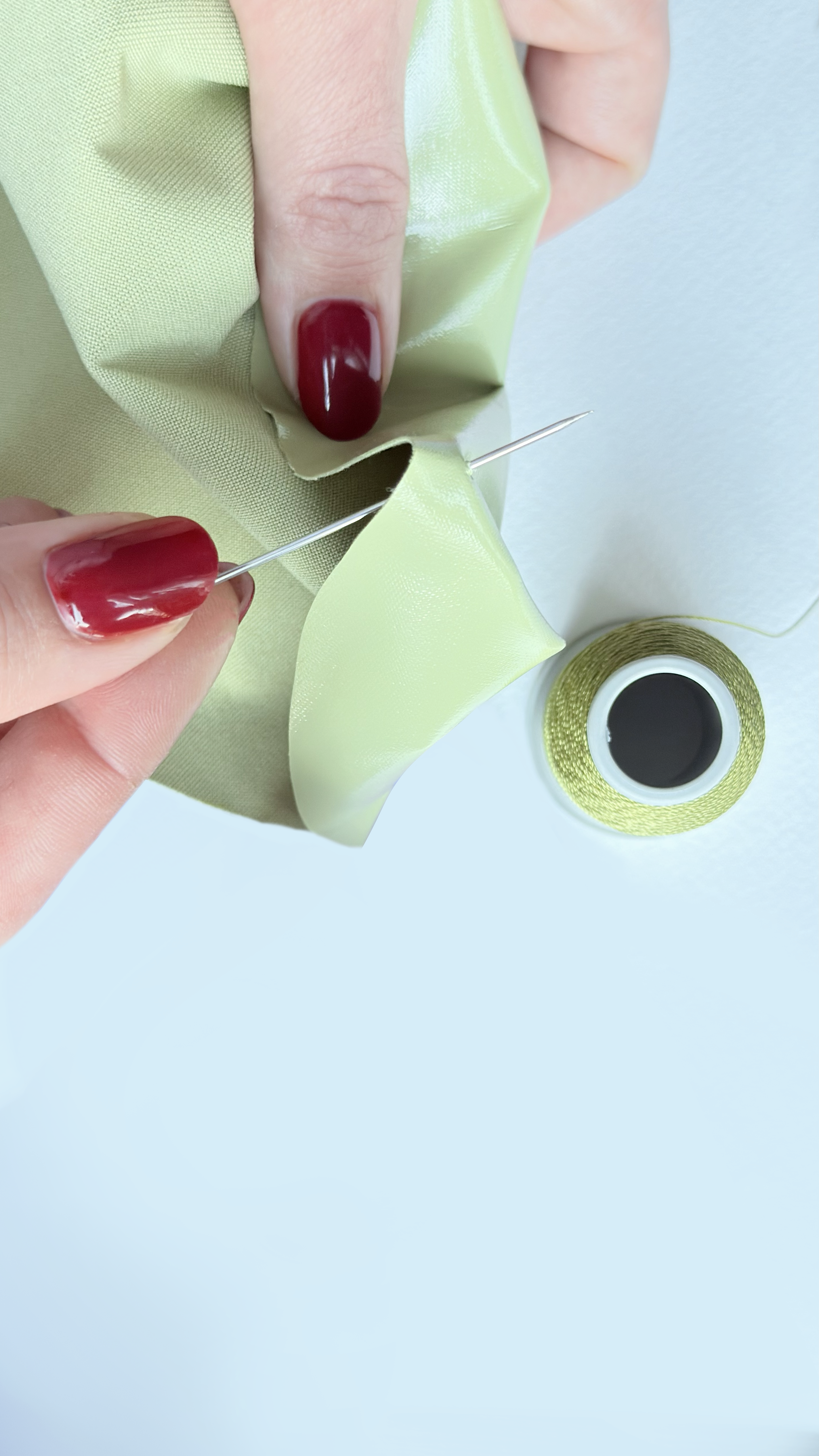 Close-up of a hand sewing green eco leather with a needle and thread during The Bulb Bag handmade crafting process in the Bucharest studio.

